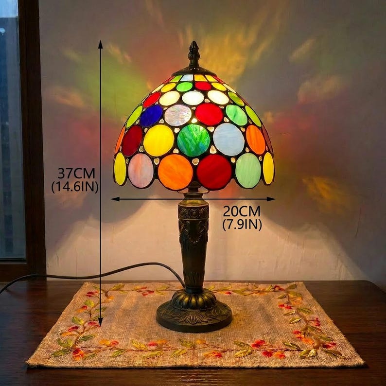 May include: A stained glass table lamp with a dome-shaped shade featuring a multicoloured polka dot pattern. The lamp has a dark metal base and stands 37 cm tall with a shade diameter of 20 cm, casting colourful light patterns.
