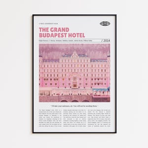Puede incluir: Un póster enmarcado de la película "El Gran Hotel Budapest" de Wes Anderson. El póster presenta un edificio rosa con el título de la película en texto rosa. El póster incluye el año 2014 y la cita: "Yo me encargo de sus maletas, señor. No las necesitará."