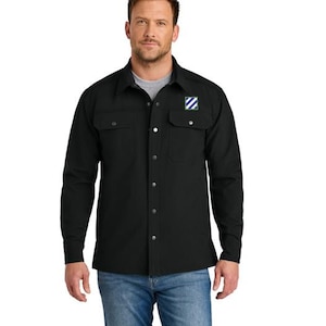 May include: Black long-sleeve button-down shirt with two chest pockets and a small patch on the left chest. The patch features a blue, white, and green striped design. The shirt is worn with blue jeans.