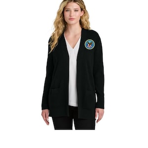 May include: A black cardigan with a patch on the left chest. The patch is circular with a blue border, an eagle, and text. The cardigan has two front pockets and is worn over a white top and black pants.