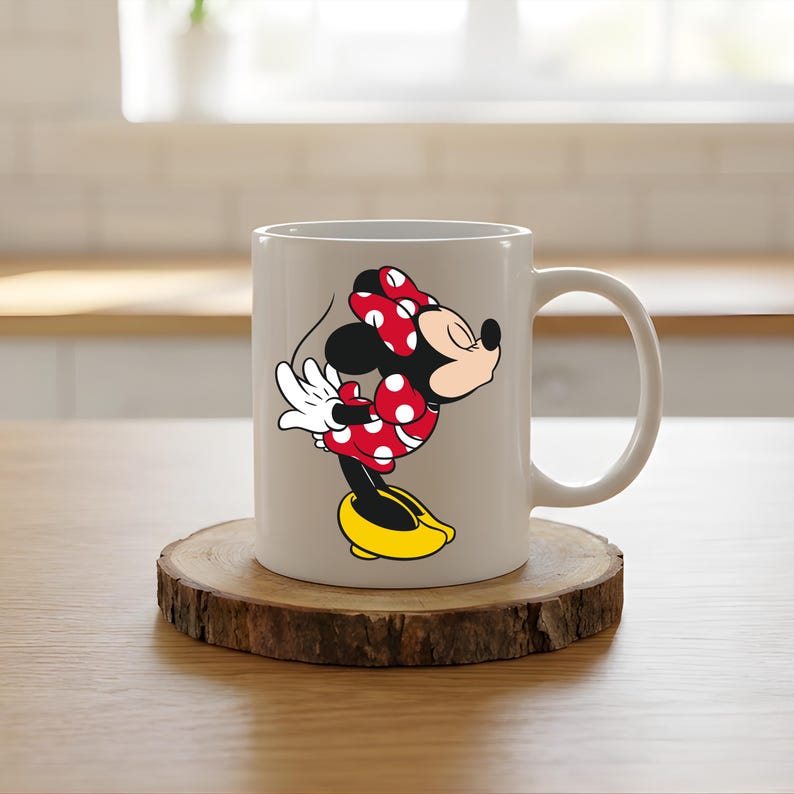 Puede incluir: Taza de cer&aacute;mica blanca con un dise&ntilde;o de Minnie Mouse. Minnie aparece con su atuendo cl&aacute;sico: un vestido rojo con lunares blancos, un lazo a juego y zapatos amarillos. La taza est&aacute; sobre un posavasos de madera.