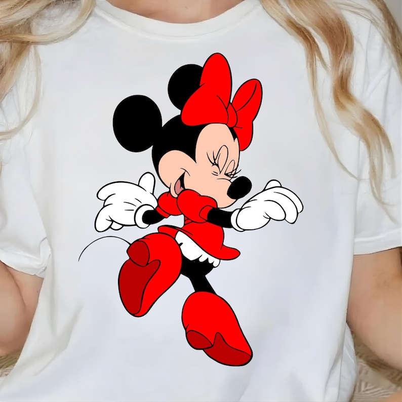 Puede incluir: Camiseta blanca con una ilustraci&oacute;n de dibujos animados de Minnie Mouse. Minnie Mouse lleva un vestido rojo, zapatos rojos y un lazo rojo. Sus orejas negras y su pelo negro son visibles. Sonr&iacute;e con los ojos cerrados y sus guantes blancos son visibles.