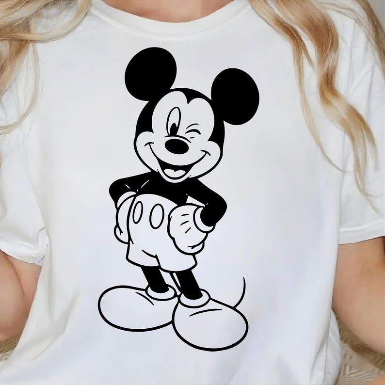 May include: White t-shirt featuring a black and white graphic of Mickey Mouse winking. The cartoon character is smiling and wearing white gloves, shorts, and shoes. The design is centered on the front of the shirt.