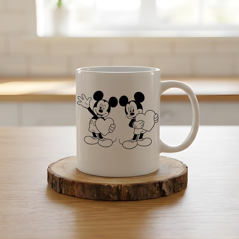 May include: White ceramic mug featuring a black and white illustration of Mickey Mouse and another character, each holding a heart. The mug sits on a round wooden coaster, with a white handle on the right side.