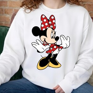 Puede incluir: Sudadera blanca con un dise&ntilde;o de Minnie Mouse. El personaje de dibujos animados est&aacute; representado con un vestido rojo con lunares blancos, un lazo a juego, orejas negras y zapatos amarillos. El dise&ntilde;o est&aacute; centrado en la parte delantera de la sudadera.