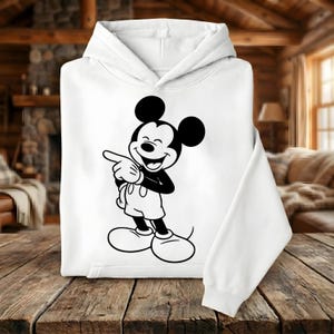 May include: White hooded sweatshirt featuring a black and white graphic of Mickey Mouse pointing. The cartoon character is smiling and wearing shorts and large shoes. The sweatshirt has a front pocket and a drawstring hood.