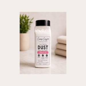 May include: A clear plastic bottle with a black cap containing white powder, labeled Camp Cozy Creations Carpet/Upholstery DUST in Black Ice scent. The label features black text, a pink accent bar, and icons, with a net weight of 16 oz.