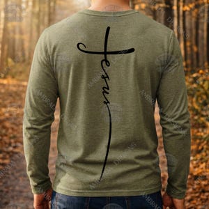 Può includere: Maglietta a maniche lunghe verde oliva con un design a croce nera e la parola "Jesus" stampata verticalmente. Il design è sul retro della maglietta. La maglietta è realizzata in un materiale morbido.