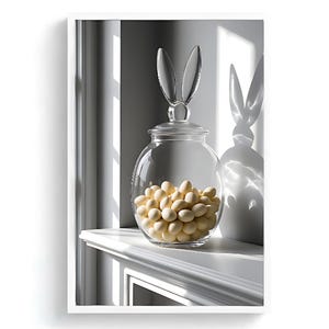 May include: A clear glass jar filled with light-colored candies, topped with a bunny ear-shaped lid. The jar sits on a white shelf, with the shadow of the jar and lid visible on the wall behind it. The image is well-lit, with a focus on the jar and its contents.