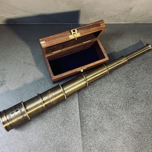 May include: A brass telescope with a wooden box. The telescope is extended and has several rings and markings. The wooden box is open, revealing a blue velvet interior. The box is made of dark wood with brass hardware.