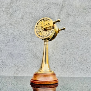 Può includere: Un telegrafo di nave in ottone con base in legno. Il quadrante del telegrafo recita "SHIP TELEGRAPH" e "Liverpool London 1866". Il telegrafo ha due maniglie e uno stelo conico in ottone.