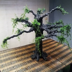 May include: A black and green artificial tree with moss-like foliage, sitting on a brown woven mat.