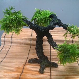 May include: A black moss-covered tree sculpture with a bonsai style. The tree is on a bamboo mat.
