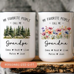 May include: Two white ceramic mugs with black handles and rims. One mug says "Grandpa" with a forest graphic, the other says "Grandma" with a floral design. Both mugs have names listed below and the text "My Favorite People - Call Me - ".
