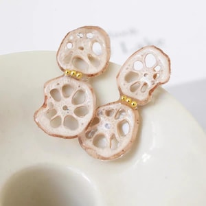 May include: A pair of earrings with a lotus root design. The earrings are light brown with a detailed, open-hole pattern and small gold accents. The earrings are set against a white background.