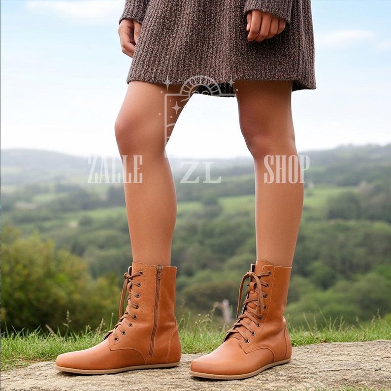 May include: Tan leather lace-up boots with side zippers. The boots have a flat sole and are worn outdoors. The boots are part of the Zalle ZL Shop collection.