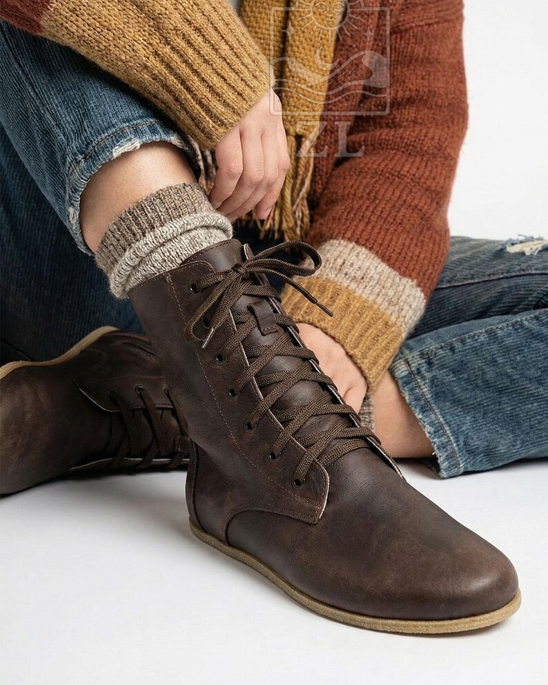 May include: Brown leather lace-up boots with a flat sole. The boots have a worn, textured appearance and are laced up with brown laces. The boots are paired with a pair of gray and beige socks. The boots are a casual style.