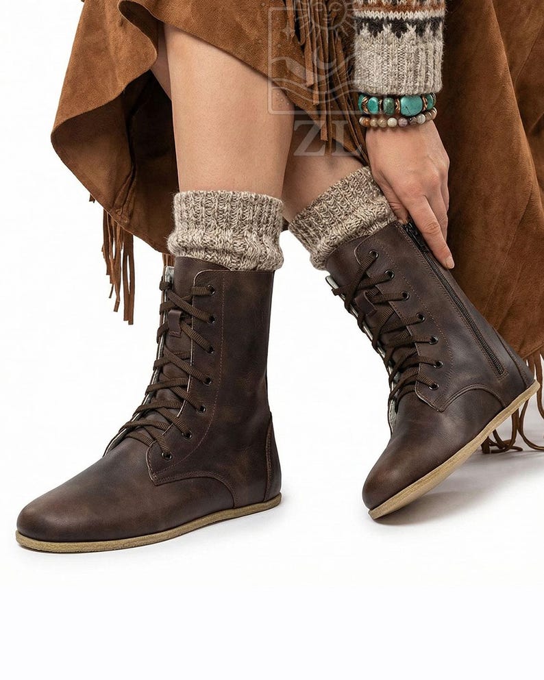 May include: Brown leather lace-up boots with a side zipper and tan soles. The boots are worn with beige knit leg warmers. The image shows a close-up of the boots and part of the person's legs.