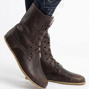 May include: Brown leather lace-up boots. The boots have a flat sole and a mid-calf height. The laces and stitching are the same color as the leather. The boots are shown from a low angle.