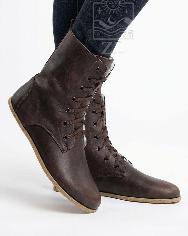 May include: Brown leather lace-up boots. The boots have a flat sole and a mid-calf height. The laces and stitching are the same color as the leather. The boots are shown from a low angle.