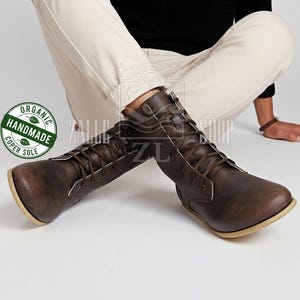 May include: Brown leather boots with a lace-up design and a light-coloured sole. The boots have a classic style and are made of a durable material. The boots are labelled "Organic Handmade" and "Coper Sole".
