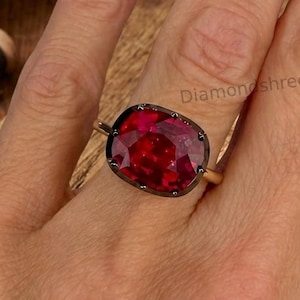 May include: A ring featuring a large, cushion-cut, deep red gemstone set in a dark metal bezel. The ring band is thin and metallic. The text 'Diamondshreejewel' is visible near the gemstone. The design focuses on the prominent red stone.