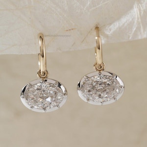 Peut inclure: Une paire de boucles d'oreilles créoles dorées avec des pierres précieuses ovales et transparentes. Les pierres sont serties dans une lunette argentée avec un design délicat et texturé. Les boucles d'oreilles sont présentées sur un fond neutre.