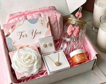 Peut inclure: Un coffret cadeau contenant une pochette en peluche rose, une carte avec le texte For You, une rose artificielle blanche, des boucles d'oreilles dorées, un collier pendentif doré, un verre avec un nœud rose et une paille, et un gommage à lèvres.