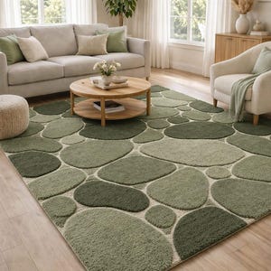 May include: A green area rug with a pebble design. The rug features various shades of green, creating a natural, organic look. The rug is placed in a living room setting with a sofa, armchair, and coffee table.