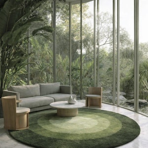 Könnte beinhalten: Ein modernes Wohnzimmer mit einem großen, runden grünen Teppich mit konzentrischen Kreisen in verschiedenen Farbtönen. Ein graues Sofa, zwei Holzstühle und ein runder Couchtisch mit weißer Platte sind im Raum angeordnet. Große Fenster bieten einen Blick ins Grüne.