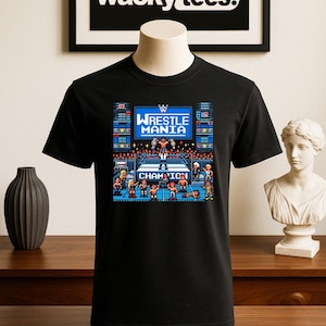 May include: Black t-shirt featuring a pixelated graphic of a wrestling match with the text "WrestleMania" and "Champion". The shirt has a crew neck and short sleeves. The brand "wacky tees" is displayed in a black frame.