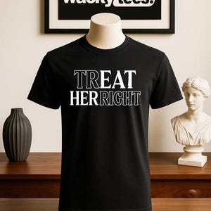 May include: Black t-shirt with the text "TREAT HER RIGHT" in white, displayed on a mannequin. The shirt is under a framed sign that says "wacky tees." A dark vase and a bust are on a wooden surface.