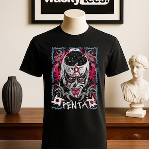 May include: Black t-shirt featuring a graphic of a masked wrestler with red, white, and blue accents, and the word "PENTA". The shirt is displayed on a mannequin. The brand "wacky tees." is displayed in the background.