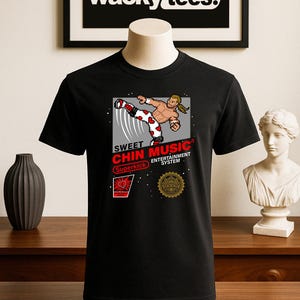 Könnte beinhalten: Schwarzes T-Shirt mit einer Grafik, die einen pixeligen Kampfsportler beim Treten zeigt. Das Design enthält den Text "SWEET MUSIC CHIN MUSIC ENTERTAINMENT SYSTEM" und "Superkick". Die Marke "wacky tees." wird oben angezeigt.