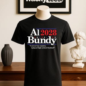 May include: Black t-shirt with the text "Al 2028 Bundy" in white, red, and blue. The shirt also features the quote, "I served my country, I played high school football." The brand "wacky tees." is displayed above the shirt.