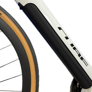 Op de afbeelding: Close-up van een wit fietsframe met een zwarte beschermhoes. De fiets heeft een zwarte band met een bruine zijwand en de merknaam "CUBE" in zwarte letters op het frame. Het wiel is zichtbaar.