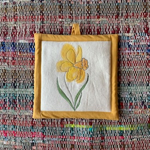 May include: Square, yellow and white pot holder with a daffodil design. The daffodil is yellow with green leaves and a yellow border. The pot holder has a small loop for hanging.
