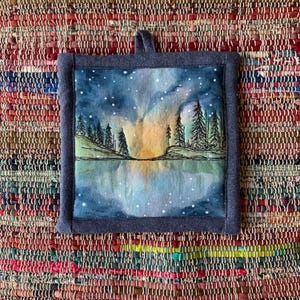 Puede incluir: Salvamanteles cuadrado y acolchado con un paisaje de acuarela con un lago, árboles y un cielo estrellado. La obra está enmarcada con una tela azul oscuro y tiene un lazo para colgar. El salvamanteles mide aproximadamente 20 cm cuadrados.