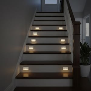 Puede incluir: Una escalera con escalones de madera marrón oscuro y contrahuellas blancas. Pequeñas luces LED blancas rectangulares están montadas en cada escalón, iluminando el camino. Una barandilla de madera oscura corre por el costado. Una planta en maceta está cerca.