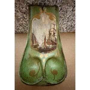 Pode incluir: Um vaso decorativo verde, em estilo vintage, com uma cena náutica pintada. O vaso apresenta um painel central com veleiros e uma moldura dourada. O vaso tem uma superfície texturizada e uma forma única.