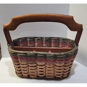 May include: Woven basket with a wooden handle and dividers. The basket features a mix of colors, including red, green, and tan. The handle is made of dark wood.