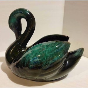 Könnte beinhalten: Eine Schwanenfigur aus Keramik mit glänzender Oberfläche in tiefen Waldgrün- und Schwarztönen. Der Schwan ist mit anmutig gebogenem Hals dargestellt, und der Körper zeigt ein gesprenkeltes, texturiertes Glasurmuster in smaragdgrünen Farbtönen.