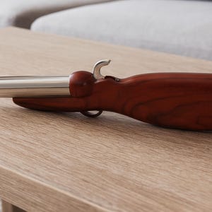 May include: A novelty bottle opener shaped like a vintage pistol. The opener features a stainless steel barrel and trigger, with a dark wood-grain handle. The opener is resting on a light-colored wooden table.