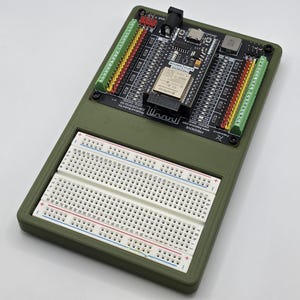 Peut inclure: Un circuit imprimé électronique vert olive avec une carte de circuit imprimé noire et une plaque d'essai blanche. La carte de circuit imprimé comporte divers composants, dont une petite puce et plusieurs connecteurs. La plaque d'essai blanche comporte des rangées de trous.