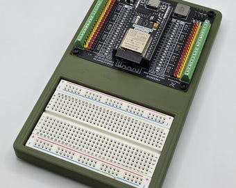 Può includere: Una breadboard elettronica verde oliva con una scheda a circuito stampato nera e una breadboard bianca. La scheda a circuito stampato ha vari componenti, tra cui un piccolo chip e più connettori. La breadboard bianca ha file di fori.