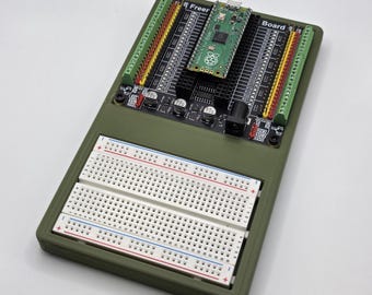 May include: An olive green electronics board with a Raspberry Pi Pico, breadboards, and various components. The board has multiple connectors and the word "Board" is visible. The word "Freer" is also visible.