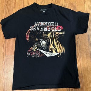 May include: Black t-shirt featuring the band name "Avenged Sevenfold" in white letters with a red accent. The shirt has a graphic design of a skull and other figures. The text "City of Evil" is also visible.