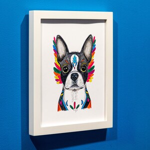May include: A framed art print featuring a Boston Terrier with colorful, stylized wings. The dog's face is black and white, with vibrant rainbow-colored accents. The artwork is in a white frame against a blue wall.