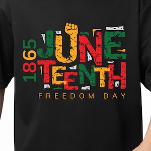 Może przedstawiać: Czarna koszulka z kolorową grafiką upamiętniającą Juneteenth. Projekt zawiera tekst "1865" w kolorze zielonym i czerwonym, "JUNE TEENTH" w różnych kolorach, zaciśniętą pięść i słowa "FREEDOM DAY".