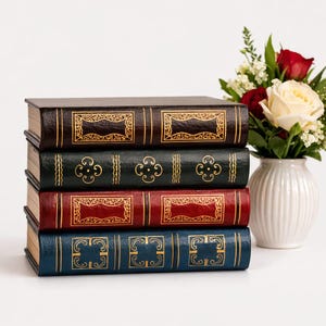 May include: A stack of four decorative books with gold embossed designs. The books are in shades of brown, green, red, and blue. A white vase with red and white roses is to the right of the books.